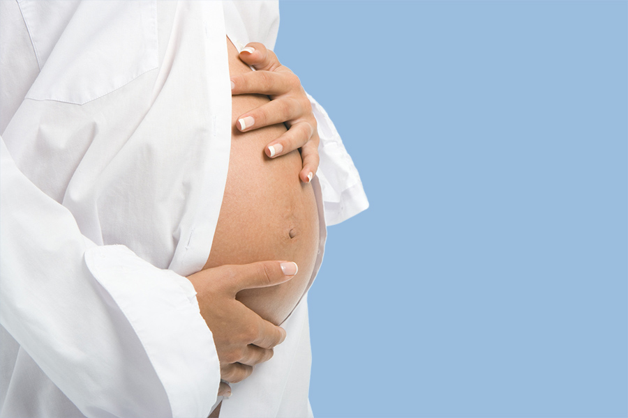 Schwangere Frau vor blauem Hintergrund berührt ihren Bauch - Frauenarzt Frauenärztin Gynäkologie Pränataldiagnostik Essen